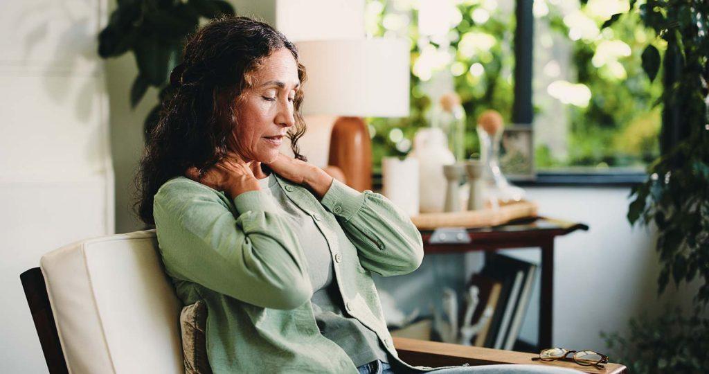 Woman holding her lower back and neck while experiencing sacroiliac joint pain and symptoms linked to lower back discomfort and SI joint dysfunction.