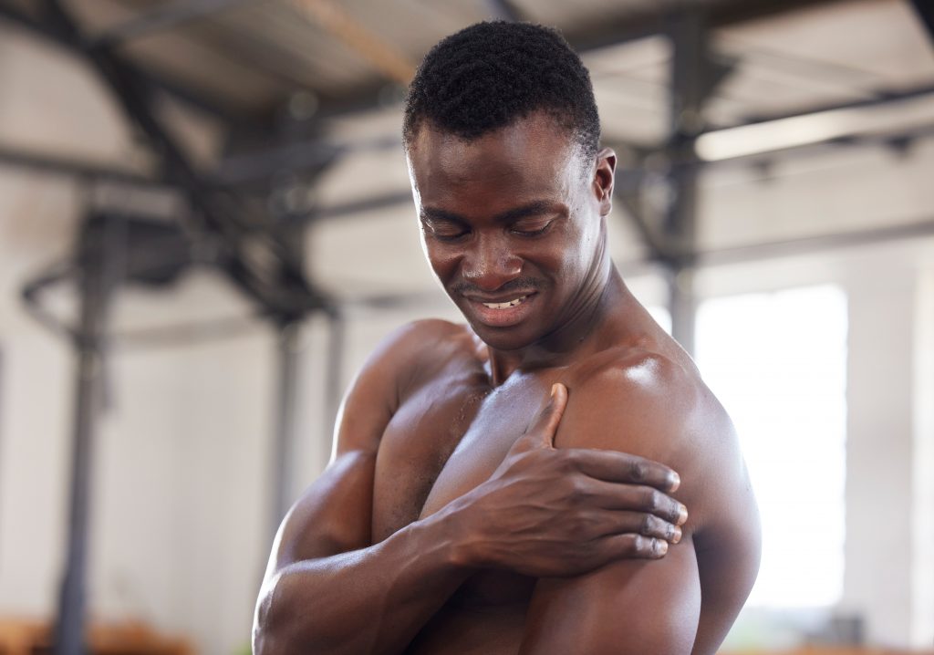 Black man, exercise and arm pain or sports injury at gym for bodybuilder training, workout or exerc.