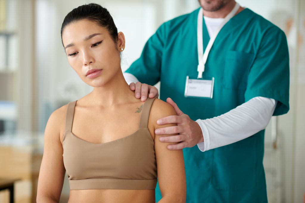 Rehab center worker palpating shoulder of sportswoman suffering with chronic pain after injury