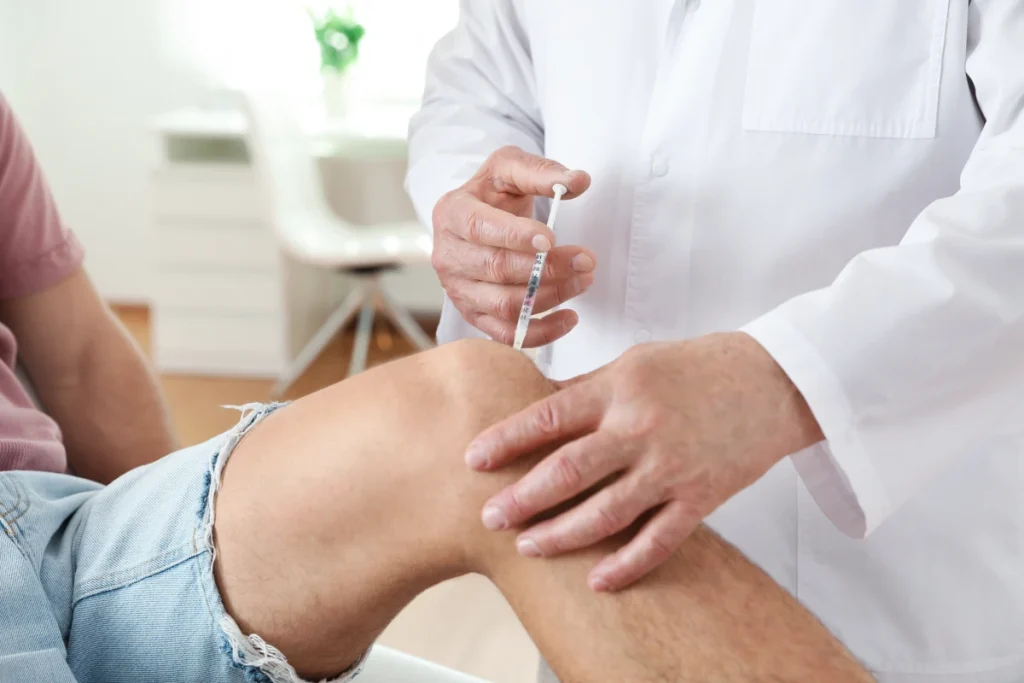 Doctor administering injection into patient knee for pain management treatment.